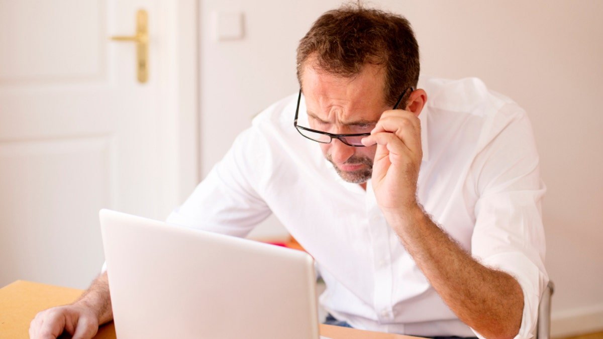 businessman sitting at a desk and looking pressed to his laptop